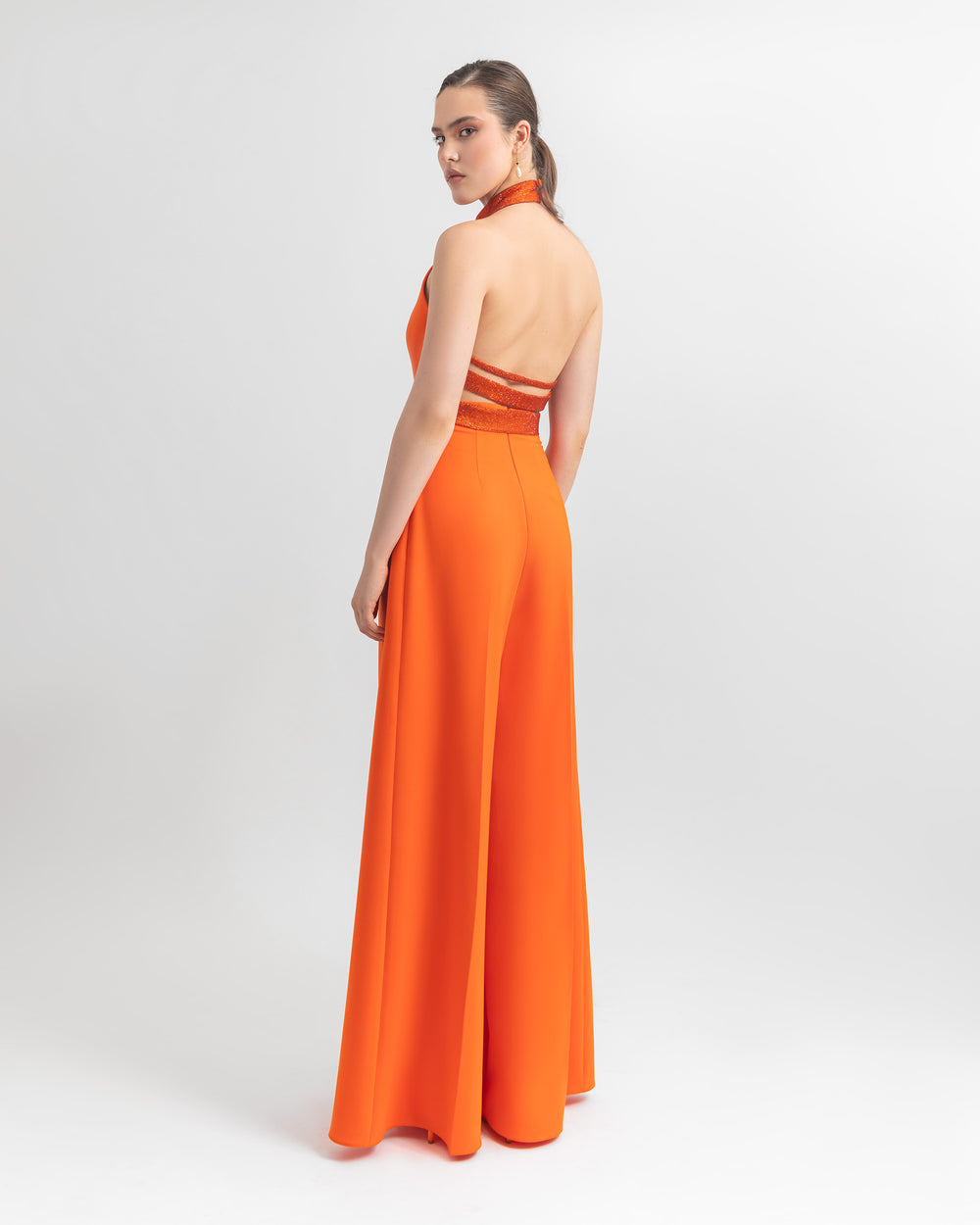 The back of an orange halter crepe top with sequins details on the neckline and the open back, paired with a wide-leg crepe pants.