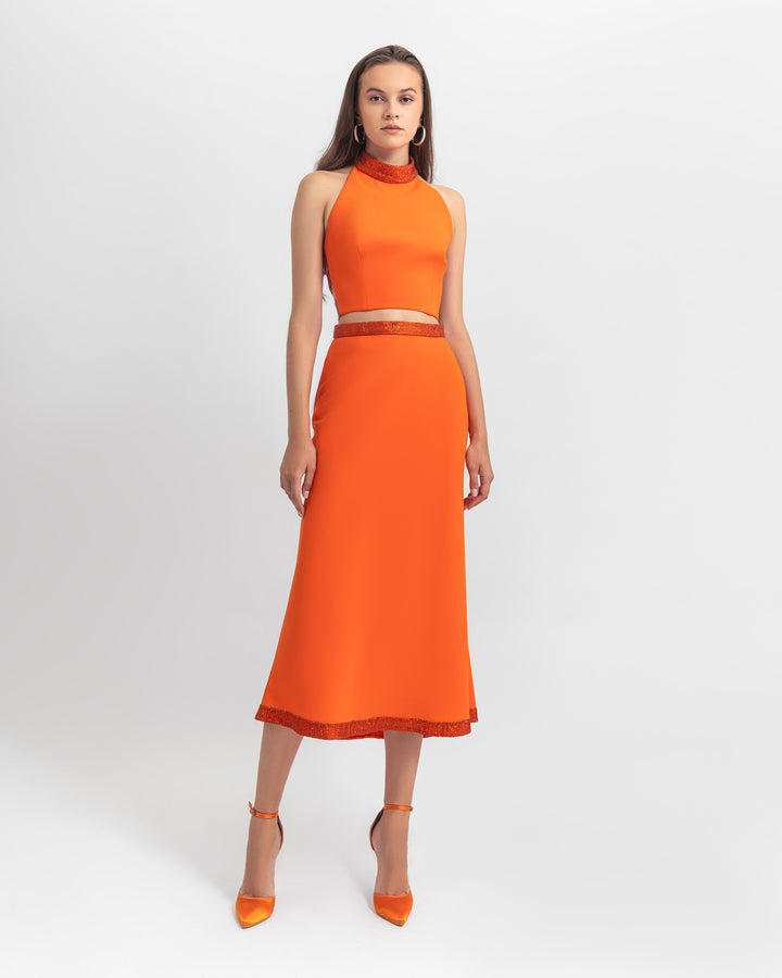 An evening wear set featuring a cropped halter neck top with a straight cut crepe orange skirt with sequin details on the waist, hemline, and neckline.