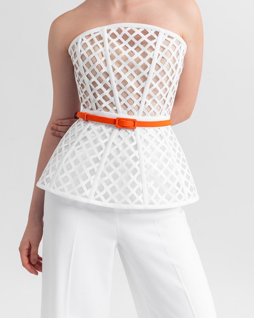 A close-up of a strapless corset-like white top, paired with straight-cut crepe white pant and a detachable orange belt.