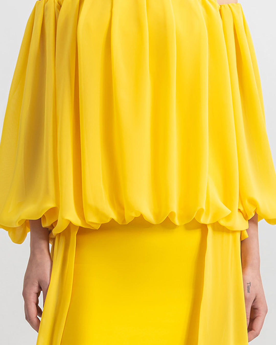 A close-up of a long sleeved loose cut chiffon yellow evening dress.