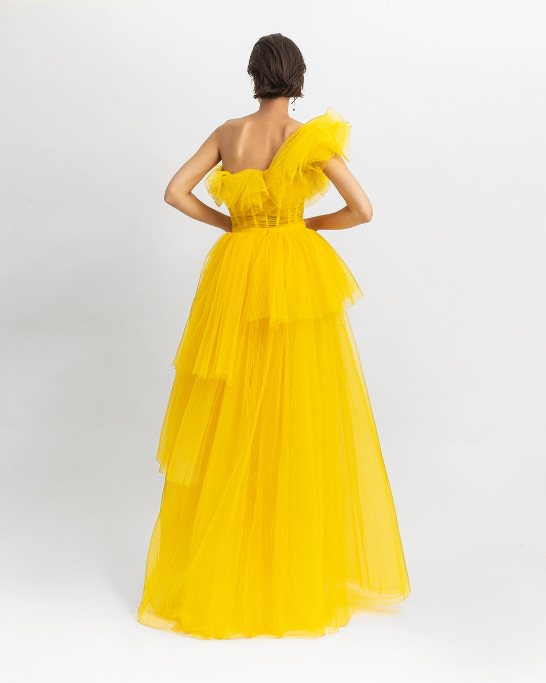 The back of a yellow one-shoulder ruffled corset tulle dress with fully pleated wide skirt.