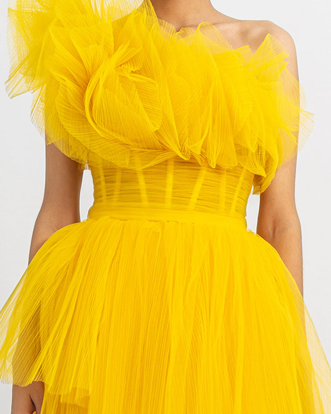 A close up of a one-shoulder yellow ruffled corset tulle dress with fully pleated wide skirt.