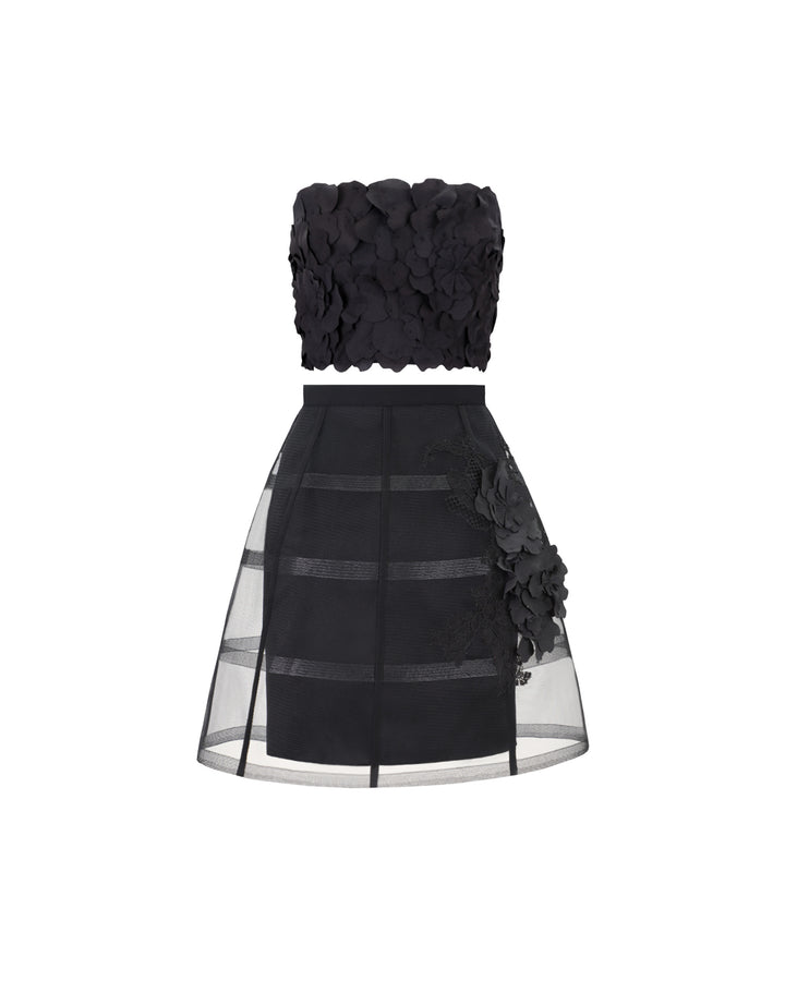 An evening wear set featuring a strapless black cropped-top with laser-cut details, paired with a cage-like black skirt with flower details.