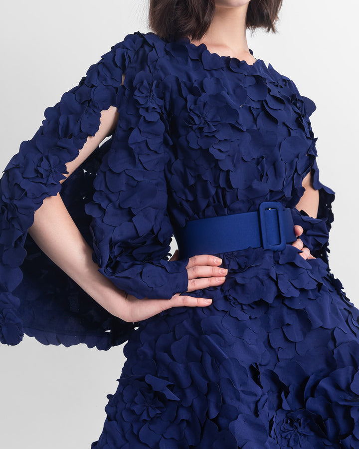 A close-up of an evening wear featuring a straight-cut laser-cut navy blue top with open-sleeve details, paired with a wide asymmetrical hemline laser-cut navy blue skirt and a detachable belt.