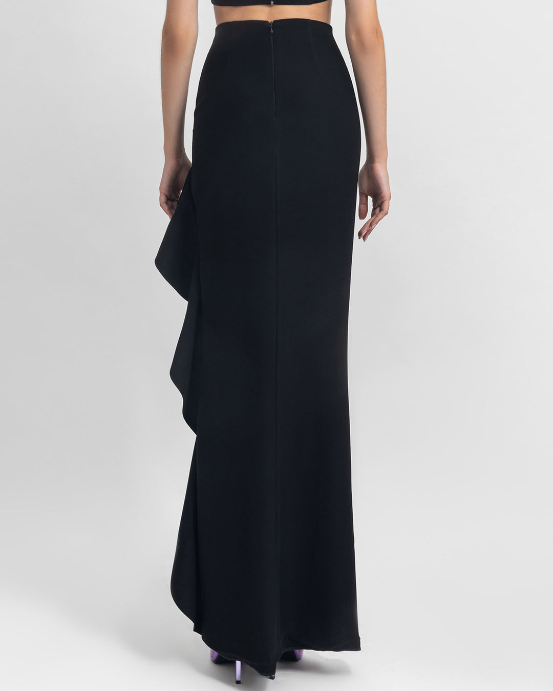 The back of an asymmetrical black crepe skirt with ruffled details and a slit on the side.