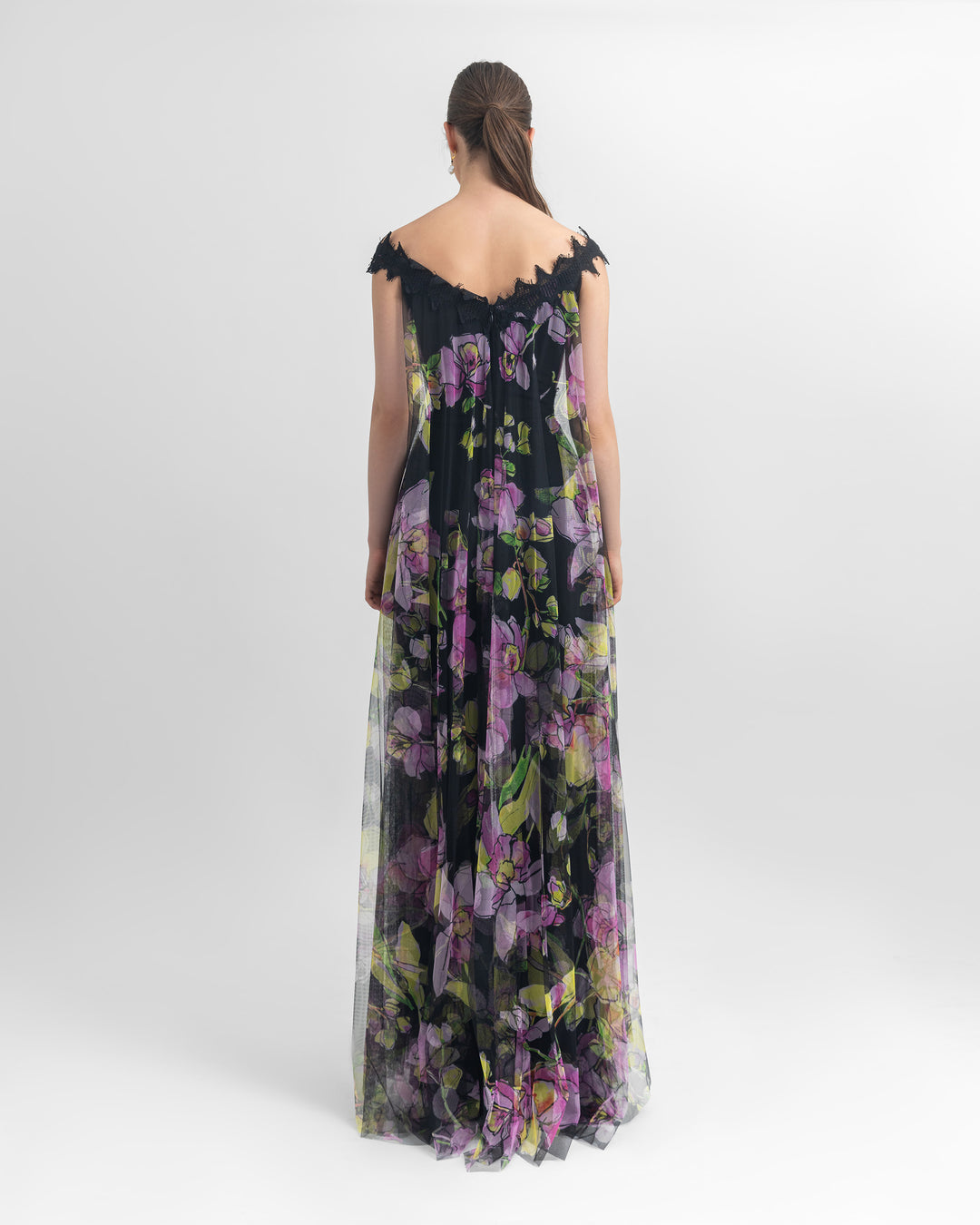 The back of an off-shoulder multicolored long floral tulle top with an open slit at the front, paired with straight-cut crepe black pants.