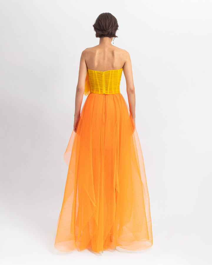 The back of a long tulle dress with an orange pleated skirt.