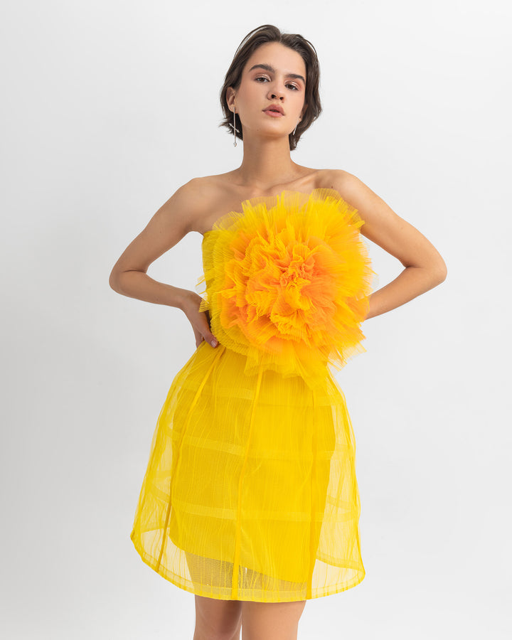 A close-up of a yellow evening wear set featuring a flower draped tulle corset, paired with a cage design mini skirt.