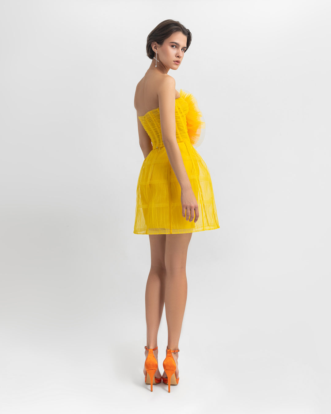 The back of a yellow evening wear set featuring a flower draped tulle corset, paired with a cage design mini skirt.