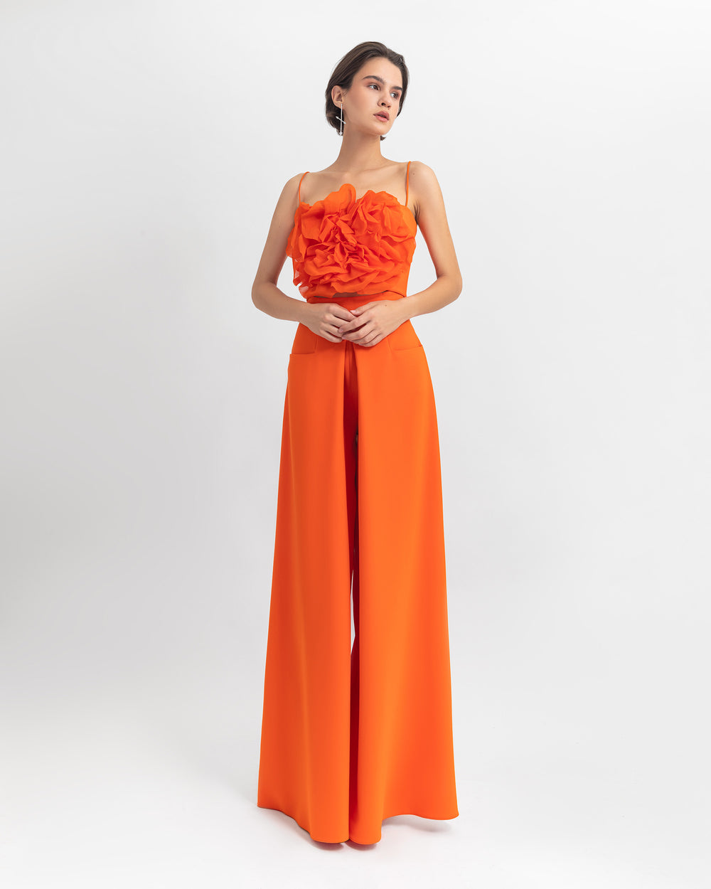 An evening wear set featuring a chiffon flower draped orange cropped top paired with a flared cut crepe pants..