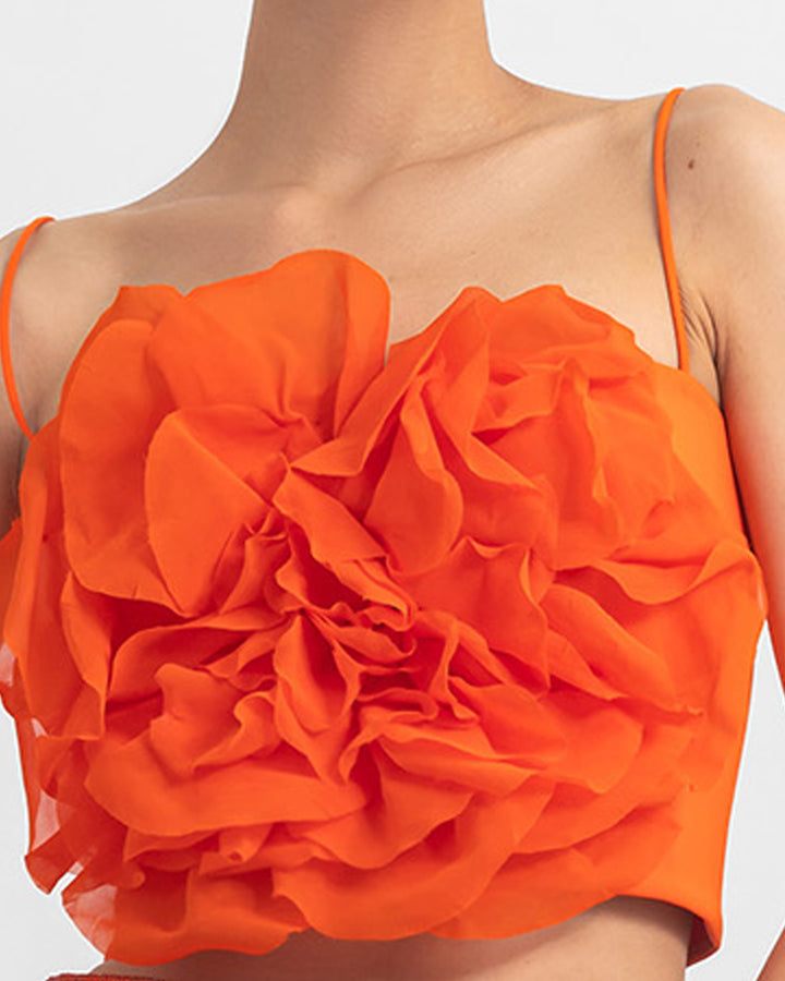 A close-up of a chiffon flower draped orange cropped top.