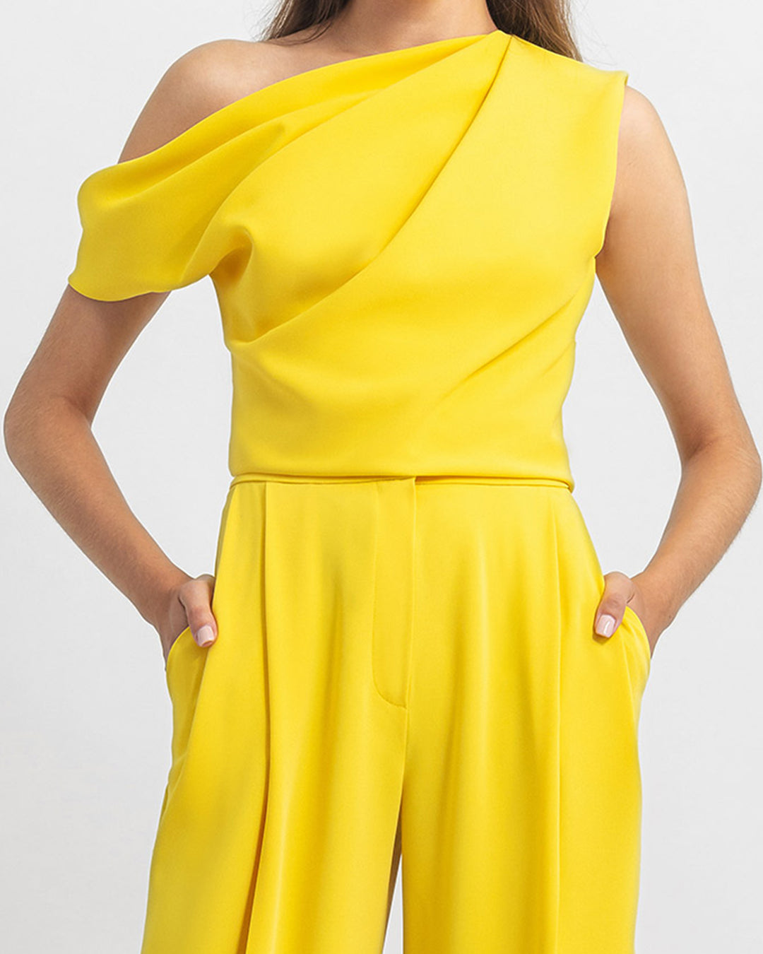 A close-up of a yellow evening wear set featuring an asymmetrical cut crepe top with draping details, paired with a straight cut crepe pants.