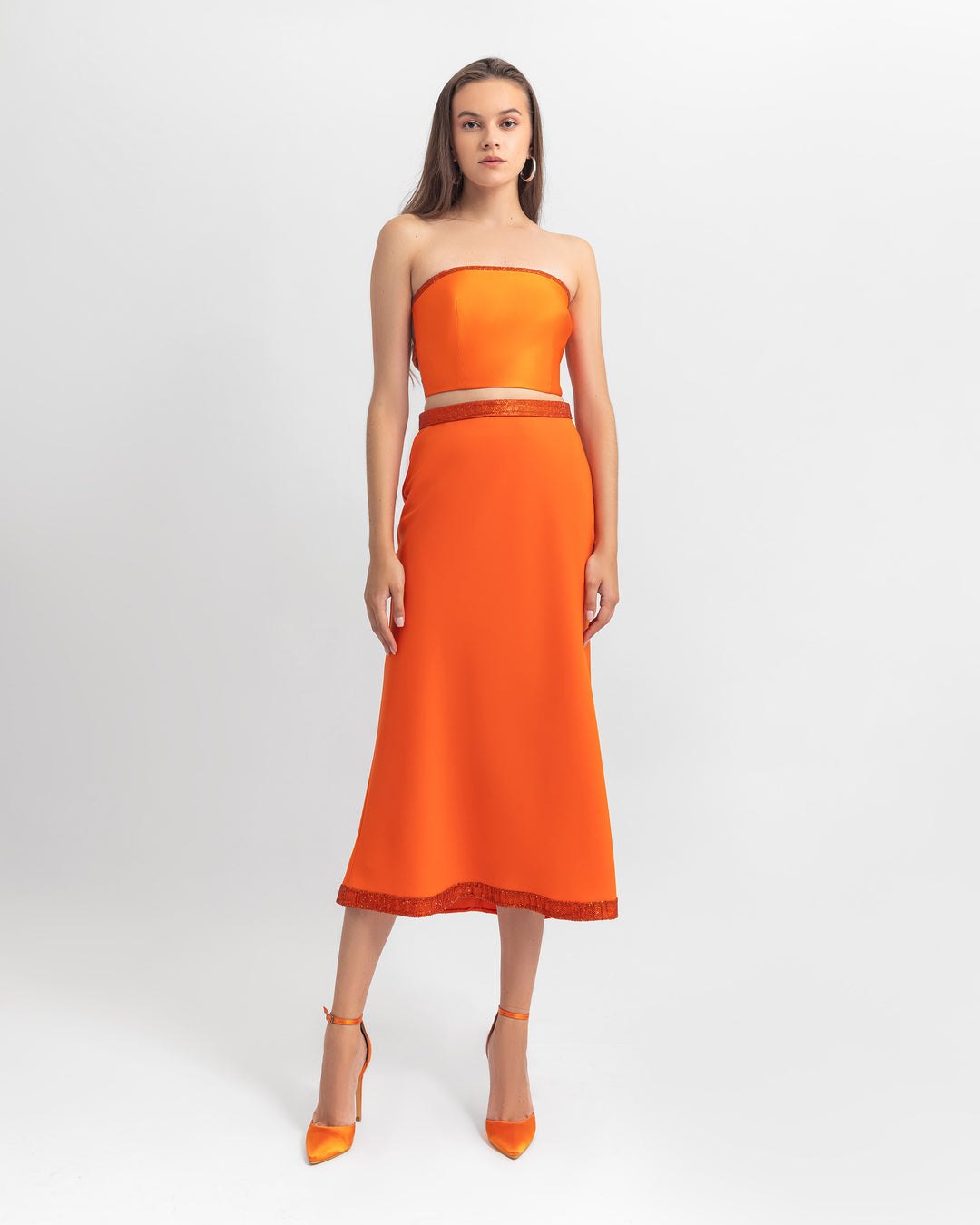 An evening wear set featuring a strapless cropped orange top with a straight cut crepe orange skirt with sequin details on the waist and hemline.