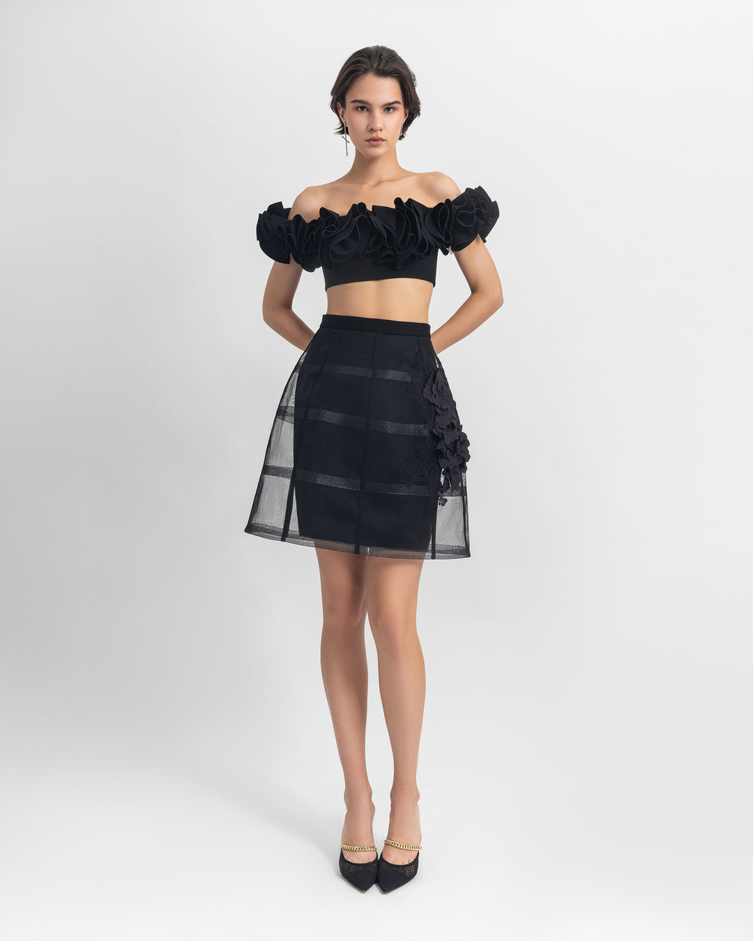 An off-shoulders ruffled crepe black crop top paired with a cage short black skirt.