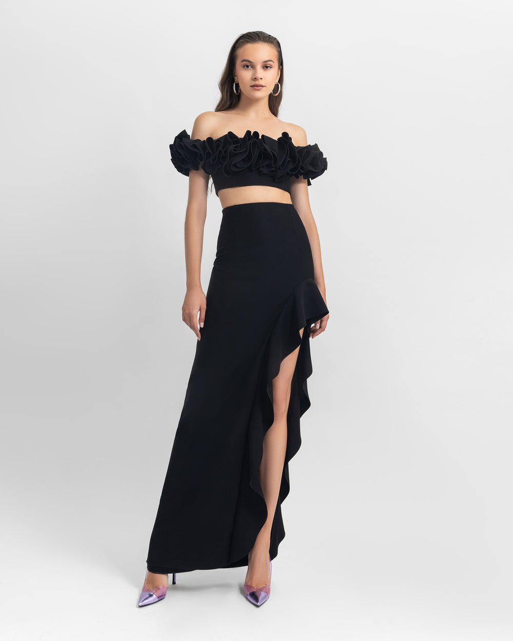 An evening wear look featuring an off-shoulders ruffled crepe crop top paired with an asymmetrical black crepe skirt with ruffled details and a slit on the side.