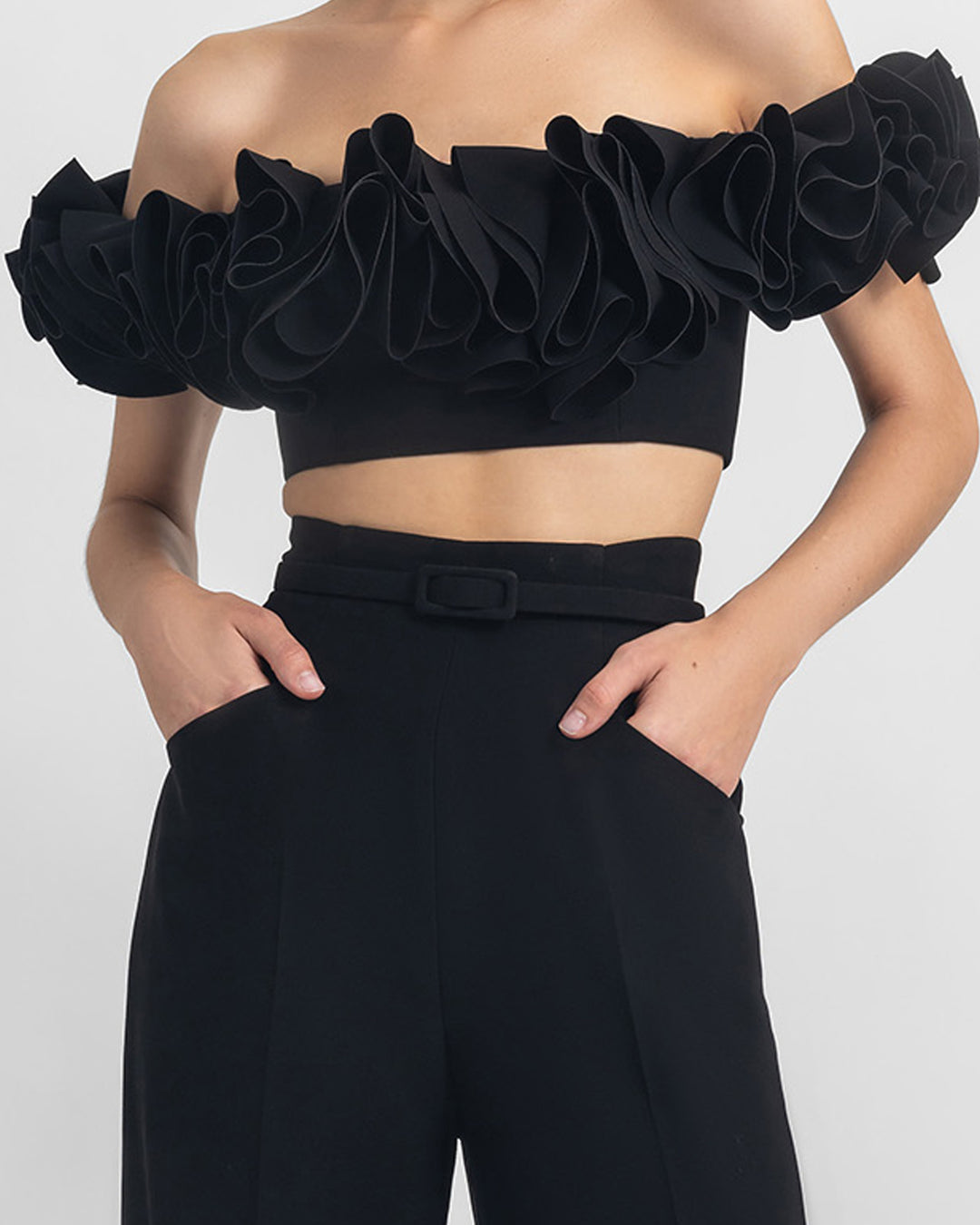 A close-up of a black evening wear set featuring an off-shoulder ruffled crepe top, paired with straight cut crepe pants and a detachable belt.