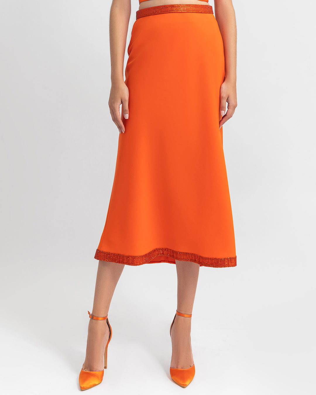 A straight cut crepe orange skirt with sequin details on the waist and hemline.