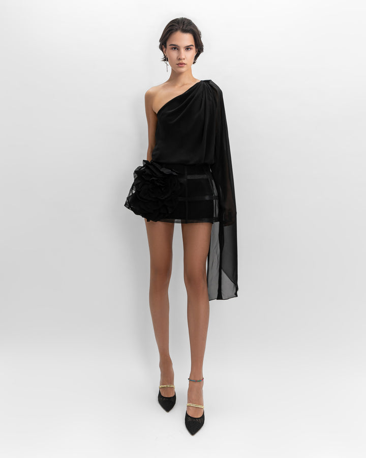 A black evening wear set featuring an asymmetrical loose-cut chiffon top, paired with a short cage-like skirt with flower details on the side.